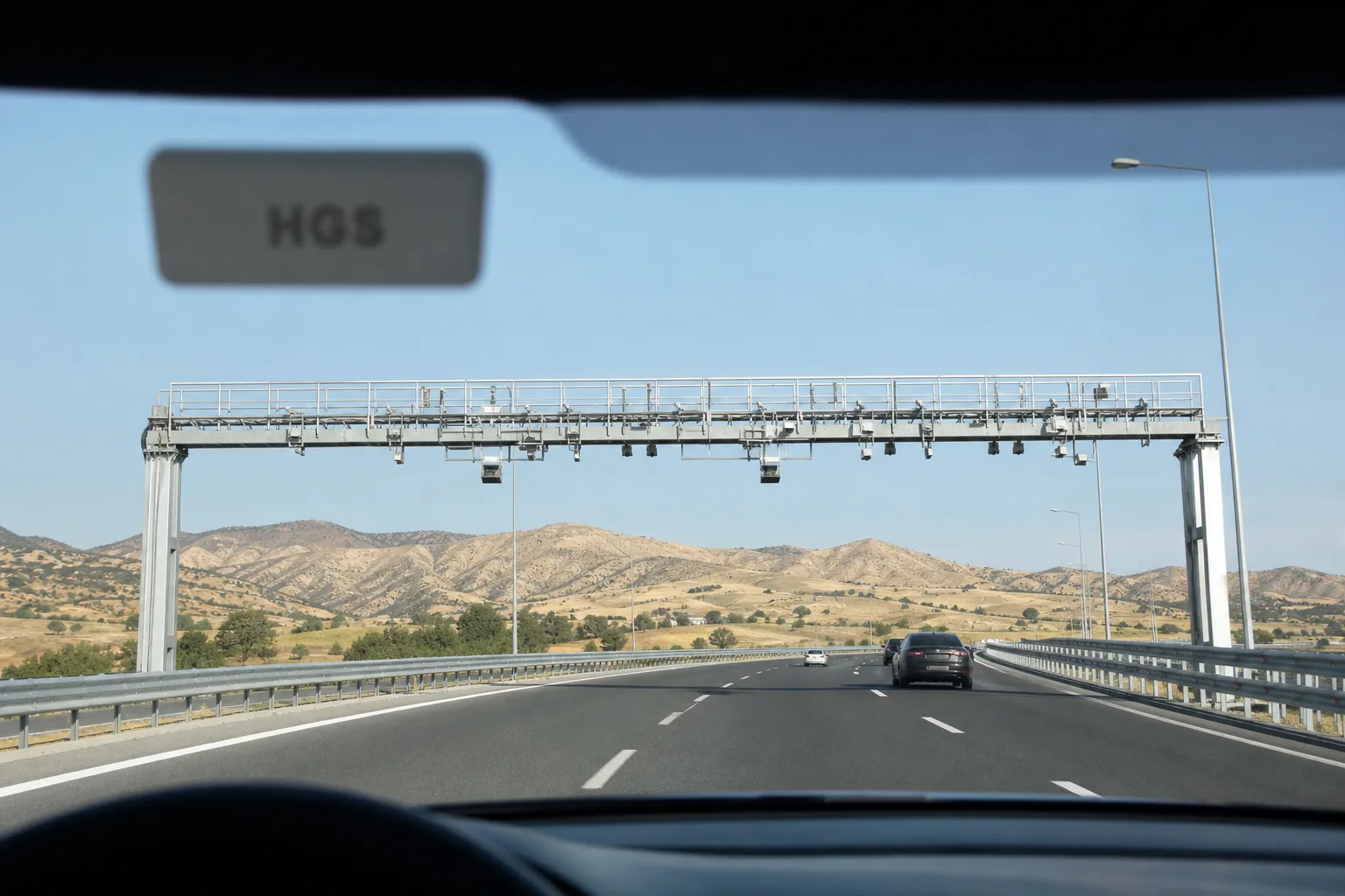 Sürücü bakış açısıyla Türkiye'de bir otoyol: ön camdaki HGS etiketi ve ileride kameralı serbest geçiş portalı.
