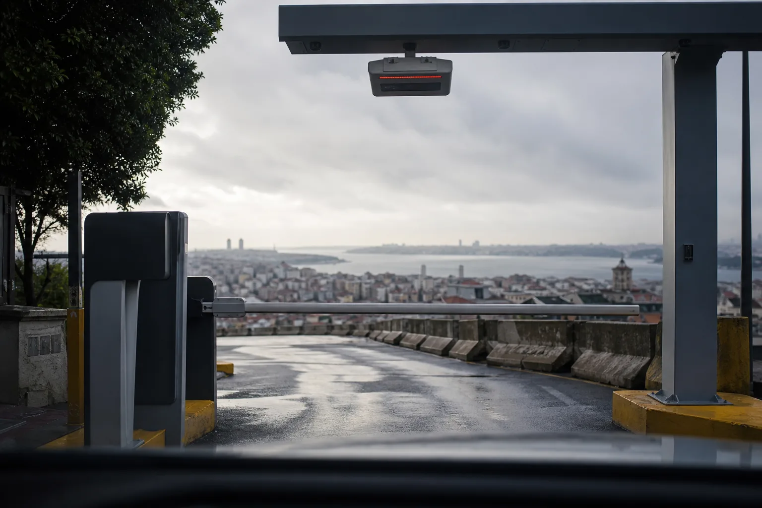 Sürücü açısından bir otoparkın açık bariyeri, şerit üstündeki plaka okuyucu ve arkada İstanbul Boğazı.