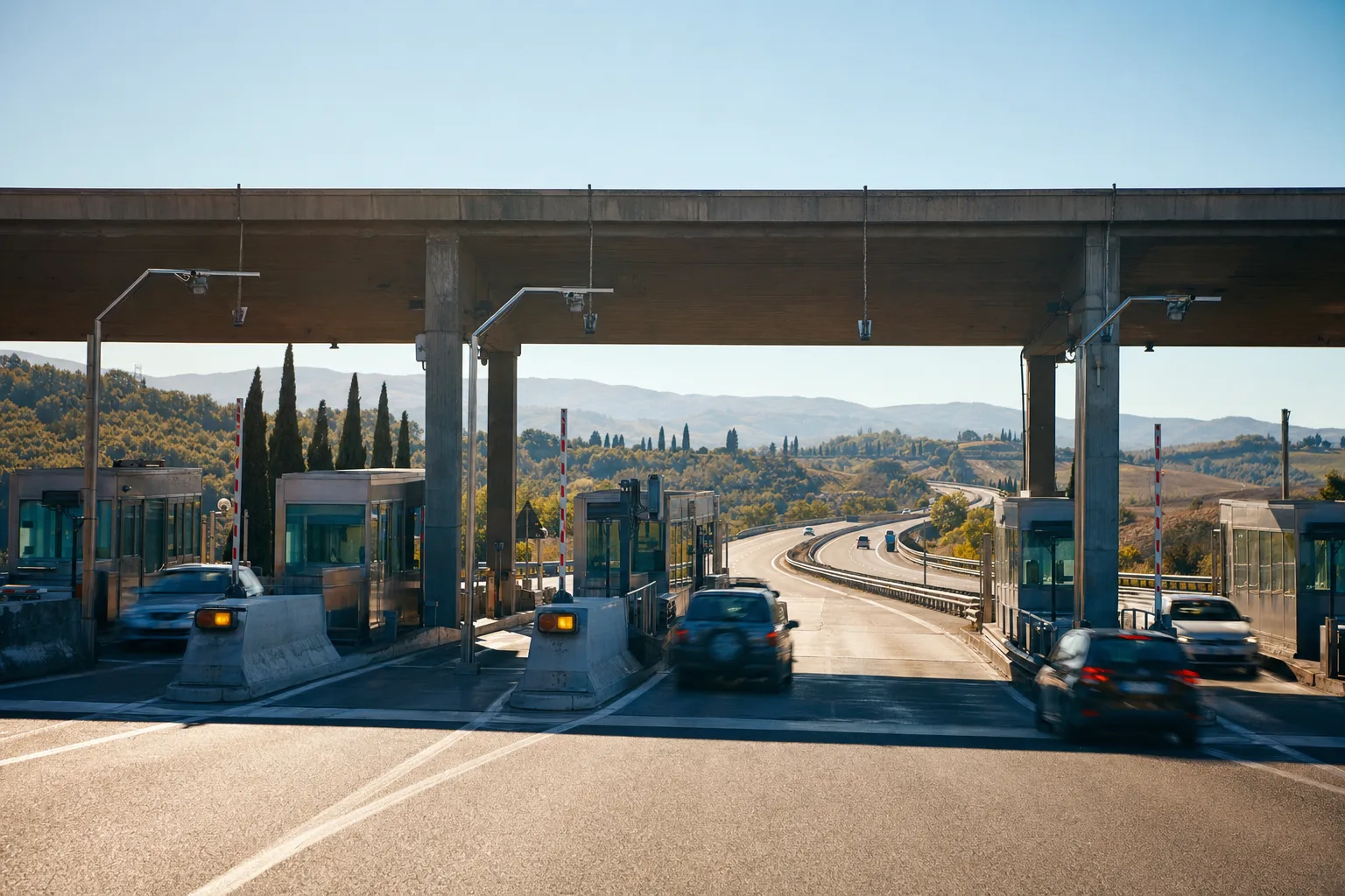 Italienische Mautstation mit Kabinen, dahinter führt die Autobahn durch die toskanischen Hügel.