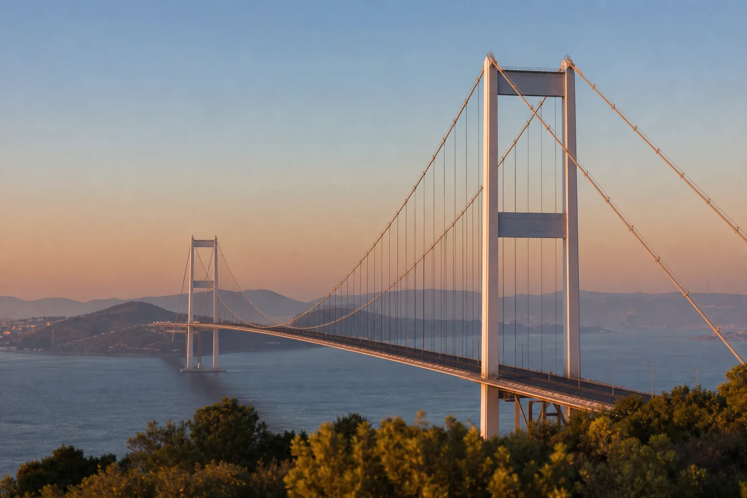 A long suspension bridge crossing a wide strait at dawn, its white towers catching the first light.