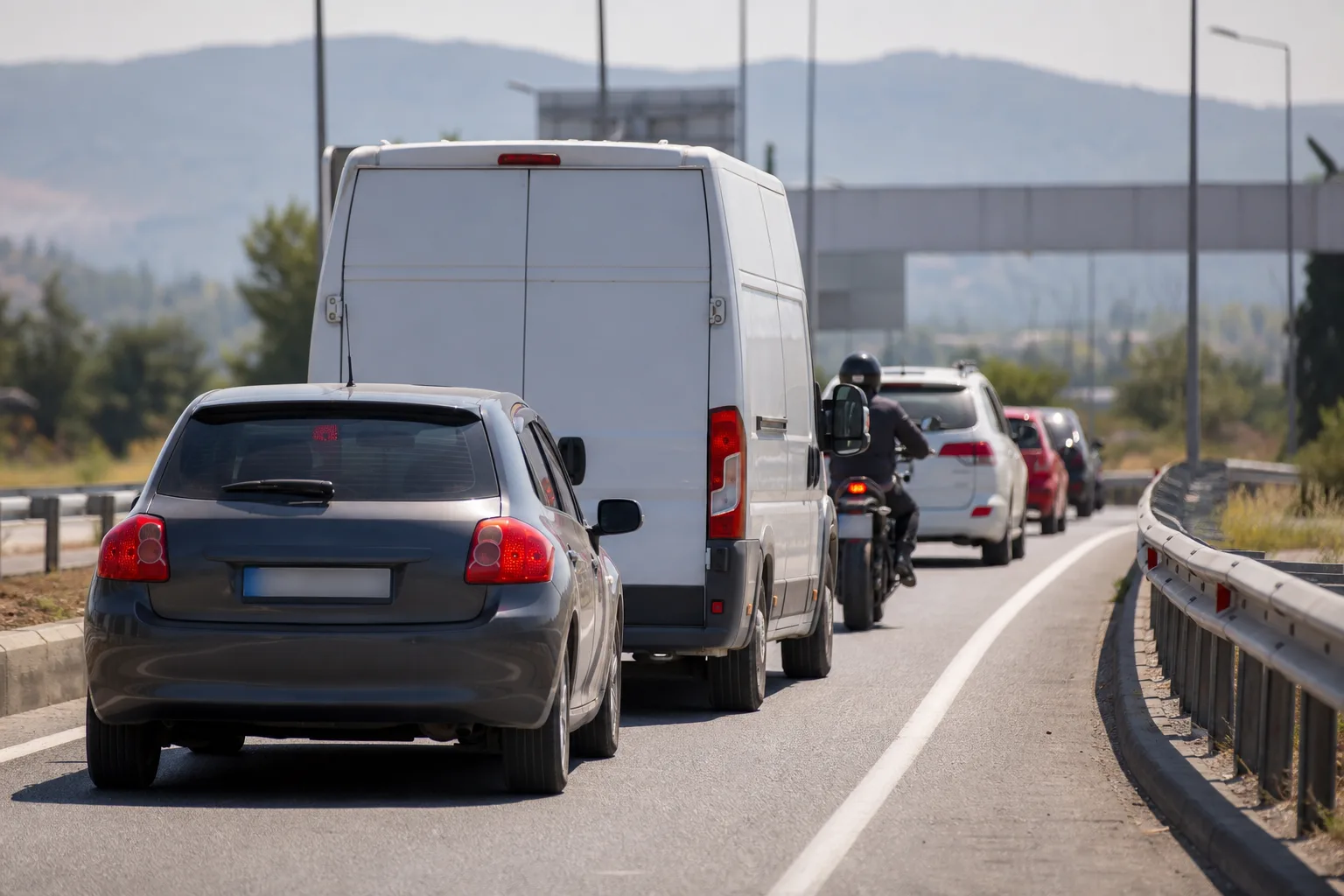 A compact car, a long-wheelbase van and a motorcycle queuing together on a Turkish highway approach lane.