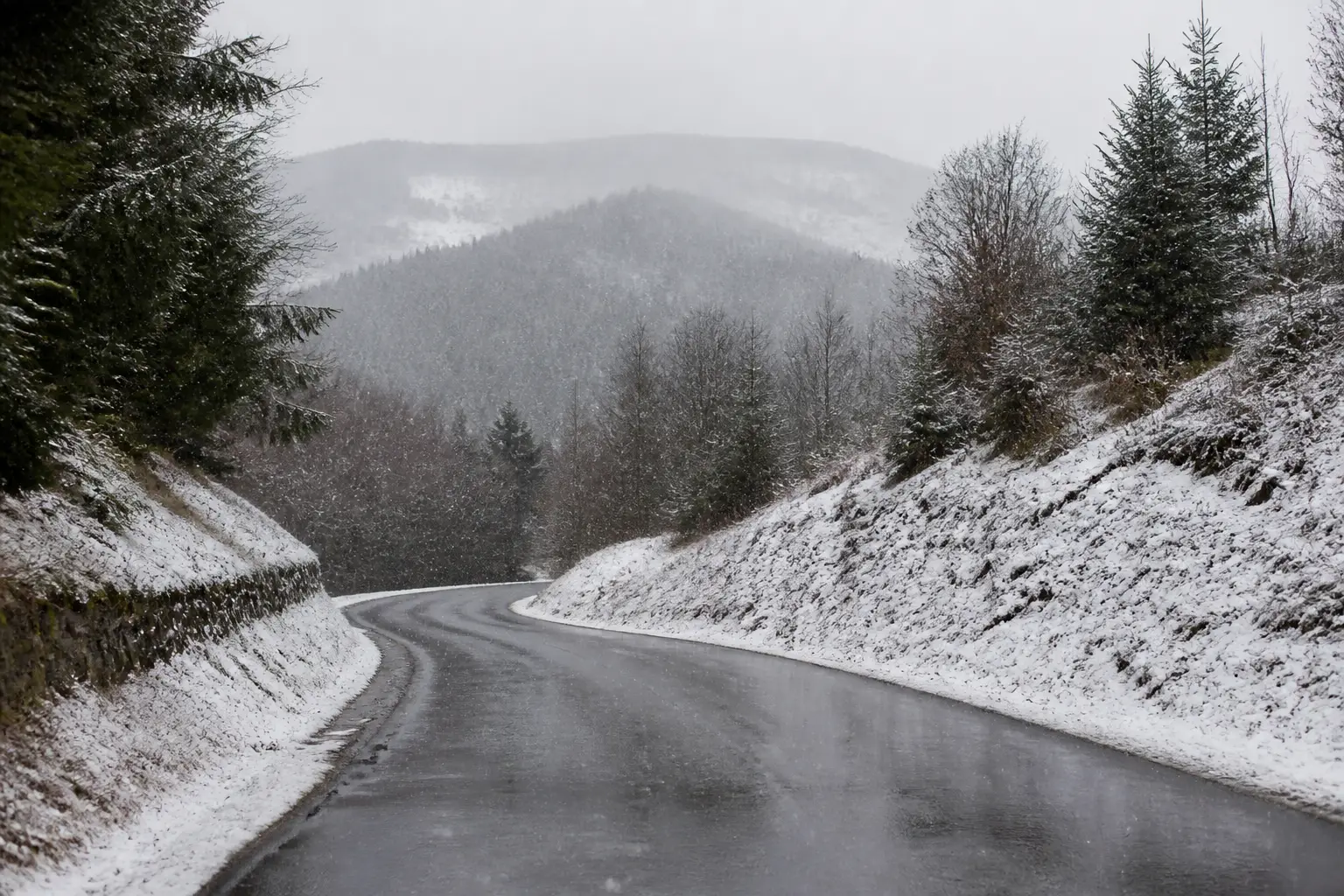 A road curving through the snowy wooded hills of the Belgian Ardennes.