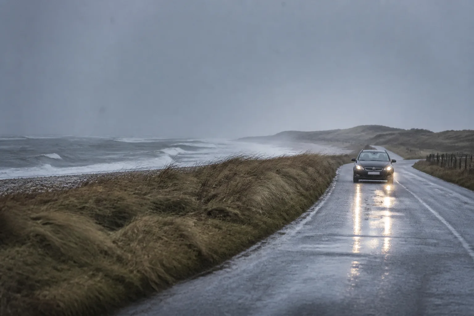 A flat Danish coastal road in wet sleet beside a grey sea.
