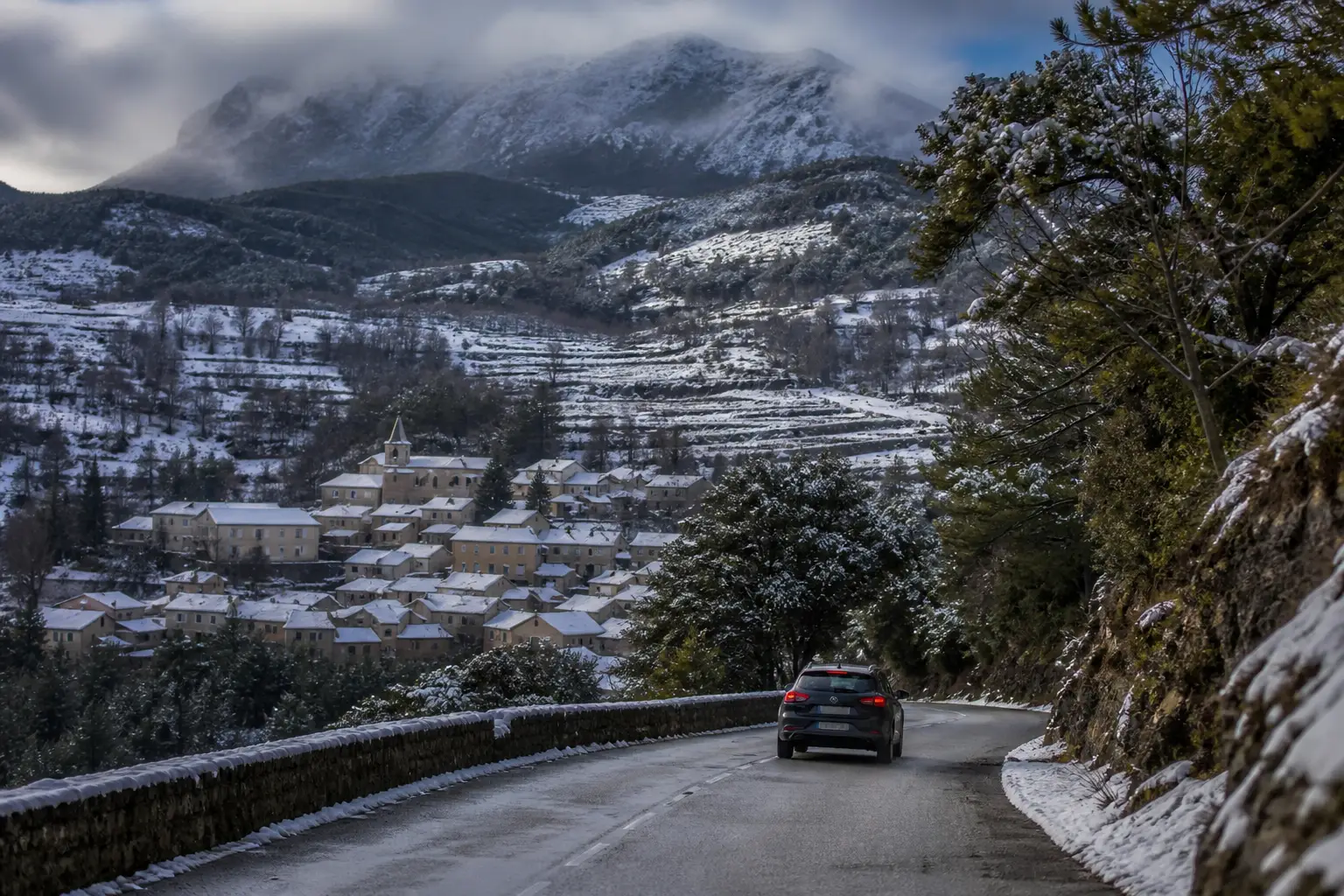 A French mountain road descending towards a snow covered valley village.