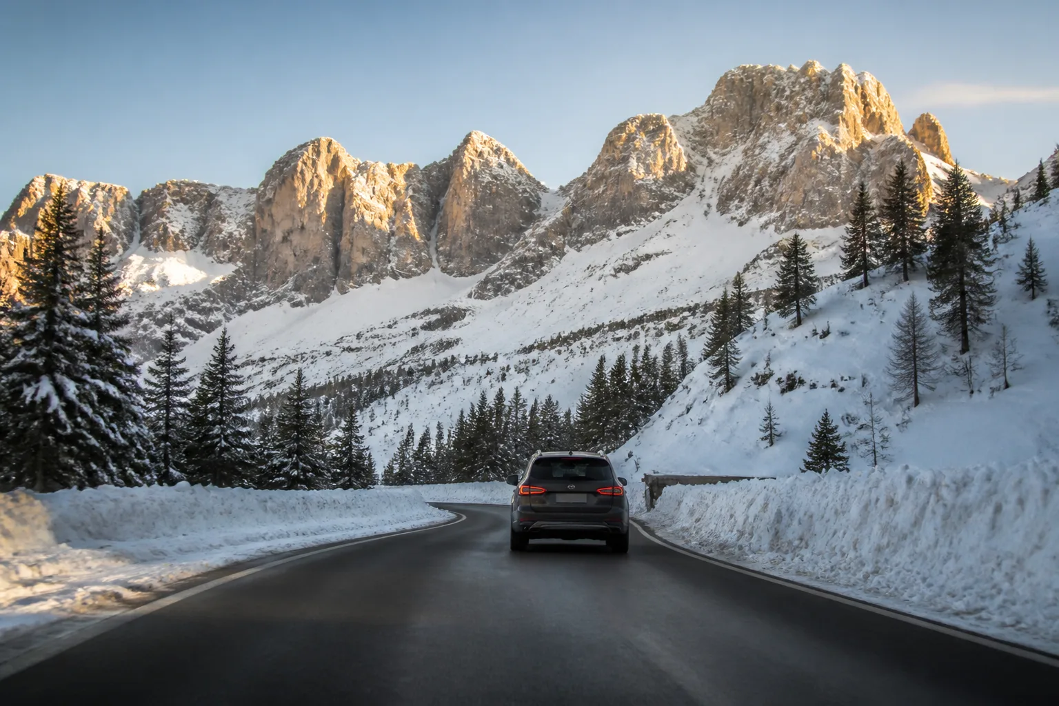 A cleared road through the snowy Dolomites with pale peaks in late sunlight.