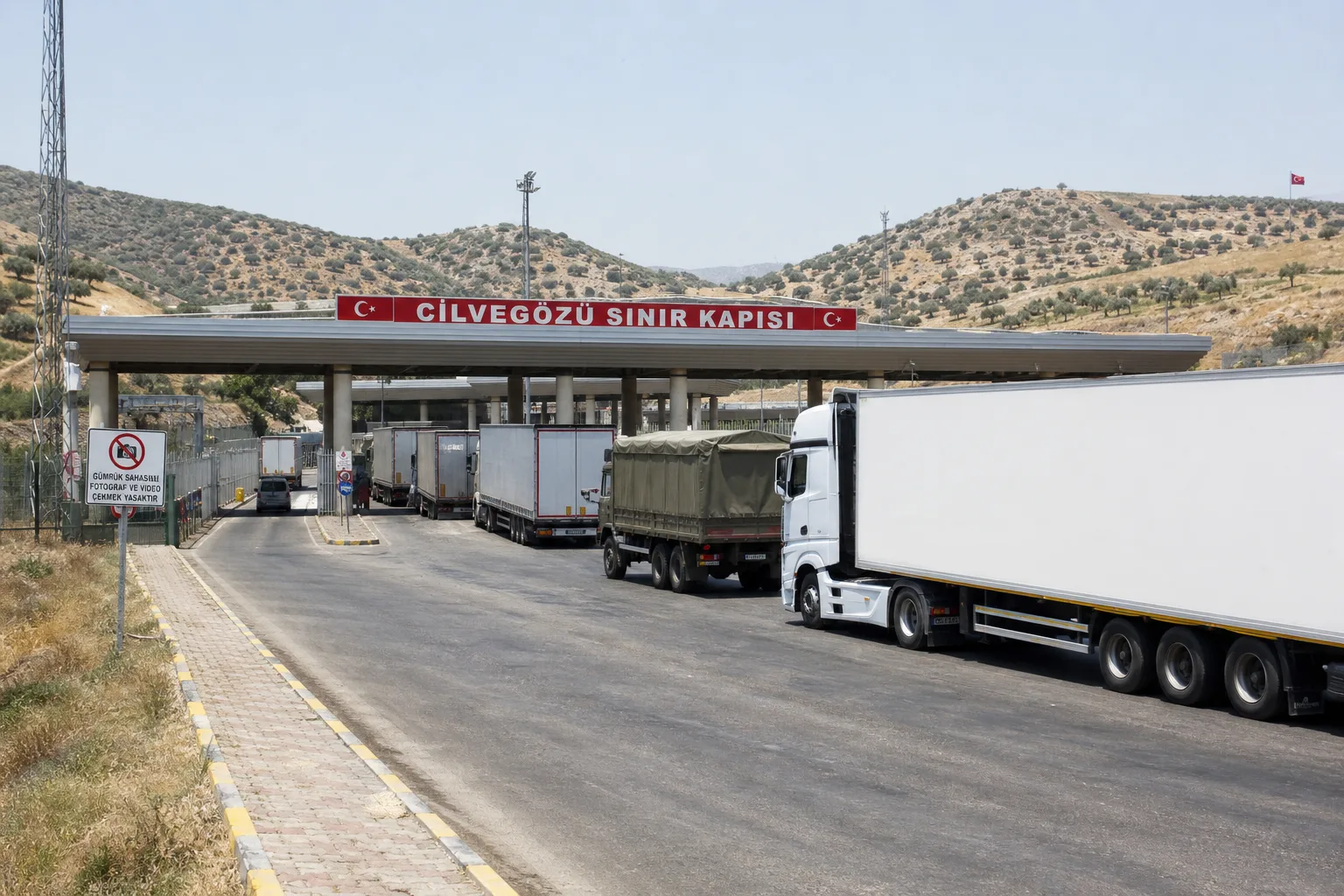 Hatay'ın zeytinli tepeleri arasında Cilvegözü Sınır Kapısı'nın uzun kanopisi ve Suriye'ye geçen tırlar.