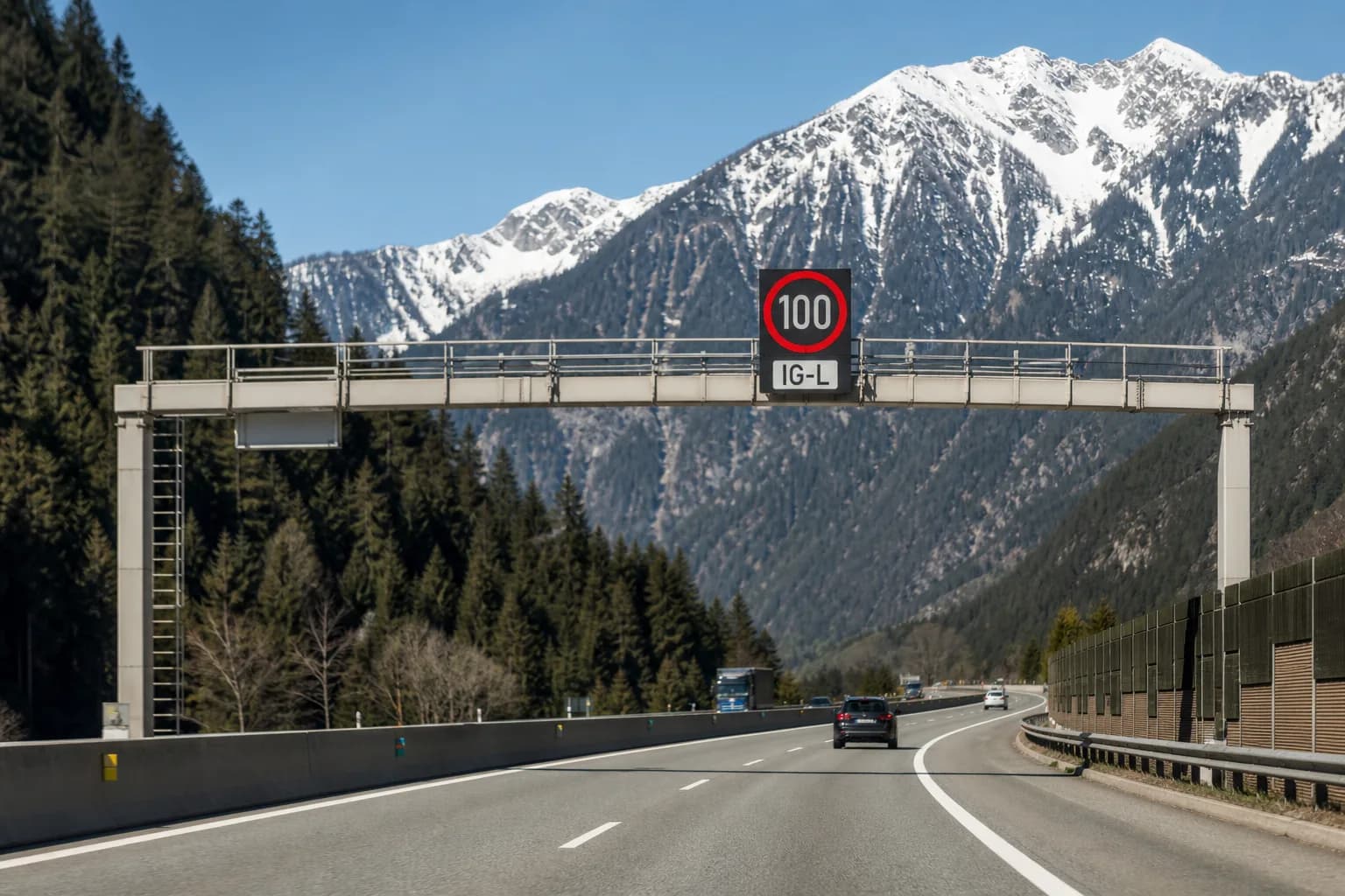 Österreichische Alpenautobahn mit Tempo-100-Schild und IG-L-Zusatztafel über der Fahrbahn.