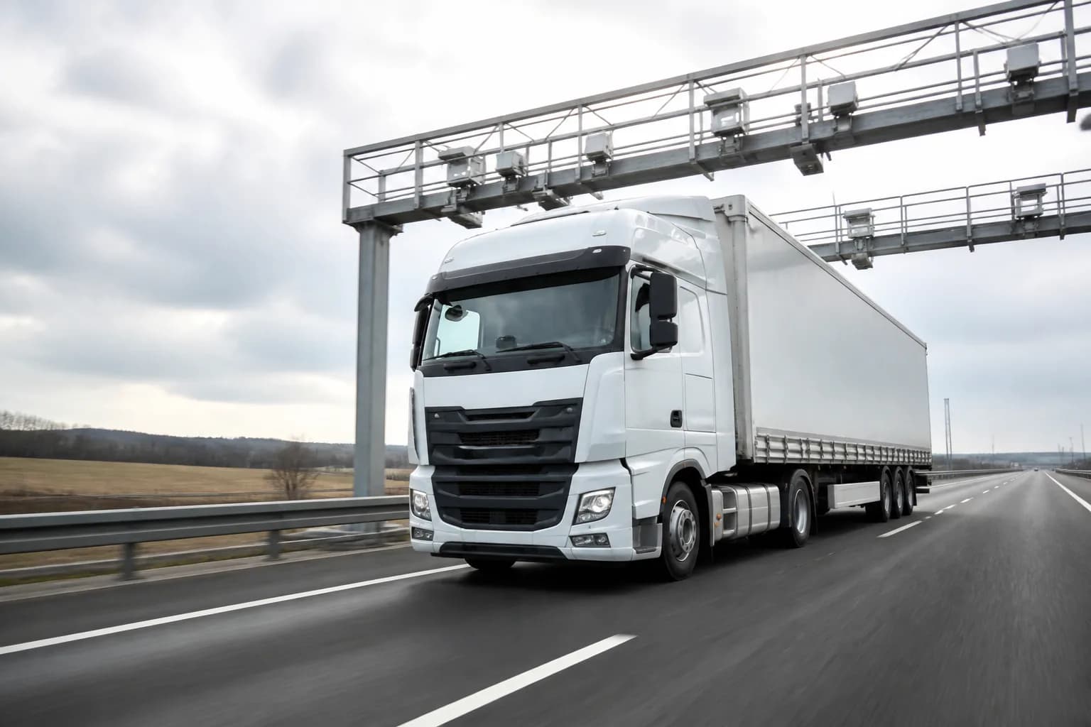 Sattelzug auf der Autobahn unter einer elektronischen Mautbrücke bei Tageslicht.
