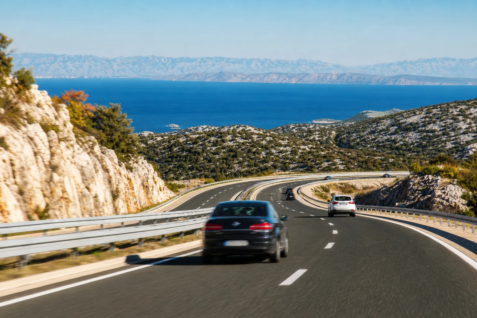 A Croatian motorway winding down white karst cliffs toward the blue Adriatic sea, evoking Croatia's motorway speed limits.