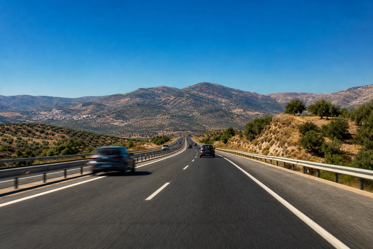 A Spanish autopista running through hills covered in olive groves under a deep blue sky, illustrating Spain's motorway speed limits.